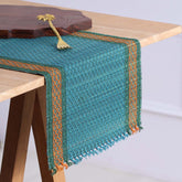 Handmade blue Madurkathi table runner woven from natural river grass with green and orange detailing styled on a 4 to 6 seater dining table