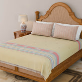 Handwoven Bawan Buti cotton bedcover in yellow styled on a wooden bed with tassel details in a contemporary bedroom setting