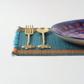 Handmade blue Madhurkathi table mats styled on a dining table with cutlery and ceramic plates, creating an elegant table setting