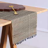 Handmade Madurkathi table runner styled on a dining table, highlighting the natural river grass weave, black tassels, and an earthy table setting