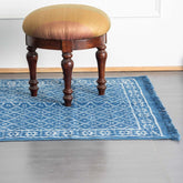 Handmade indigo diamond floral dhurrie rug styled in a reading corner, showcasing traditional weaving and block printing