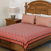Marigold jaal pink block printed bedcover styled on a bed with coordinated cushions, creating a warm and inviting bedroom setting