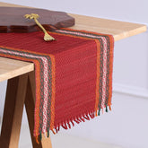 Handmade red Madhurkathi table runner styled on a dining table, highlighting the natural river grass weave, colourful borders, and elegant table setting