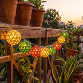 Bright multicoloured spherical bamboo string lights lit up and strung across a balcony area outdoor set up for an evening celebration.