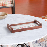 Hand embroidered wooden serving tray with pink floral motifs and green leaves on white fabric, styled with tea cups and snacks on a tabletop