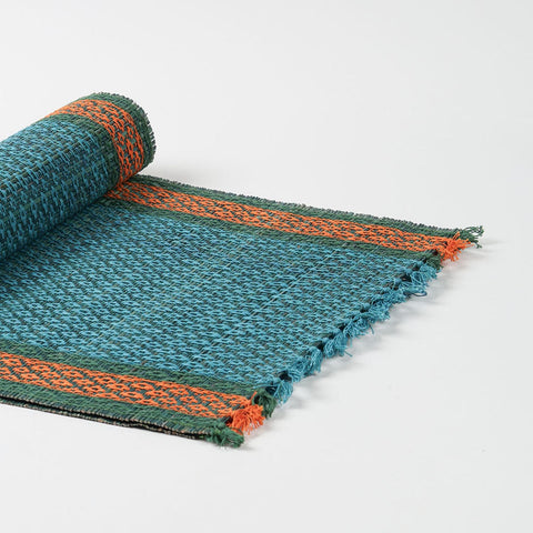 Angled view of a handmade 4 to 6 seater Madhurkathi  dining table runner  in blue, showcasing flexible natural fibre weaving and colourful woven borders
