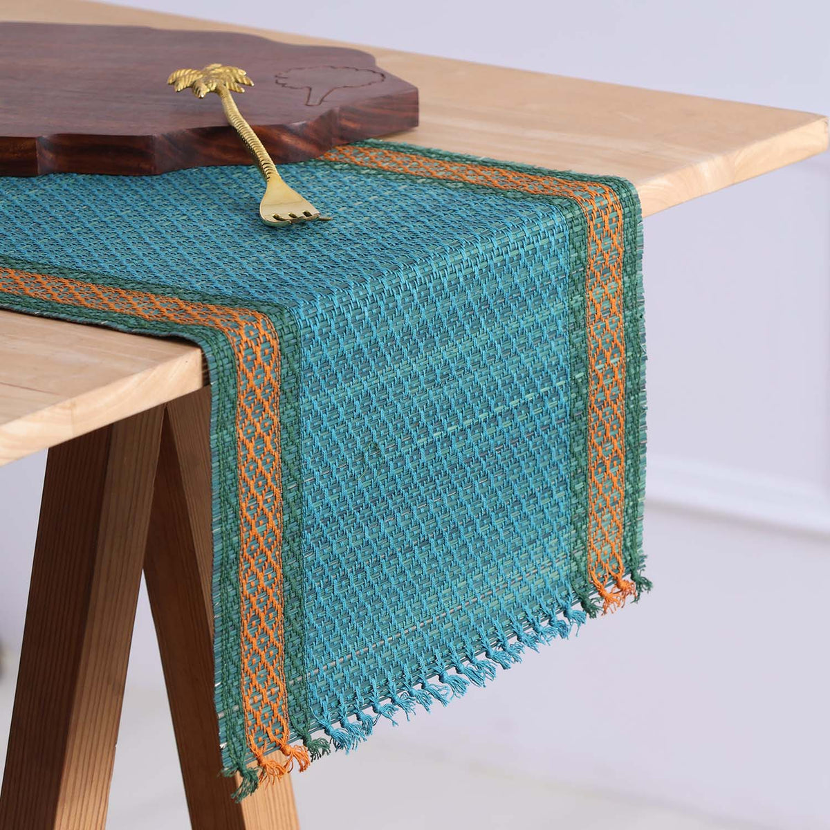 Handmade blue Madurkathi table runner woven from natural river grass with green and orange detailing styled on a 4 to 6 seater dining table
