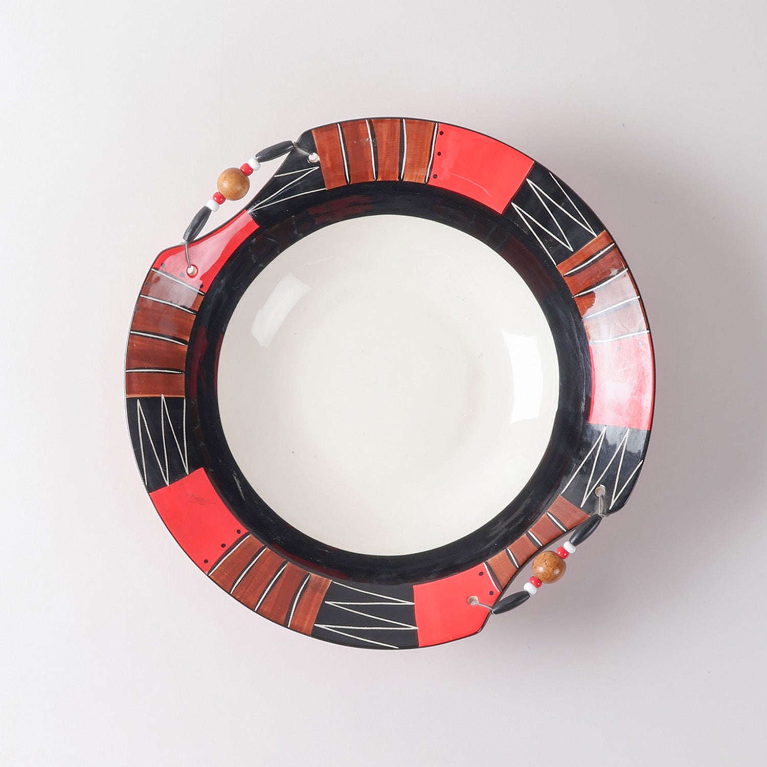 Top view of a handmade ceramic bowl with a white interior, bold African-inspired geometric rim patterns, and decorative wooden bead accents