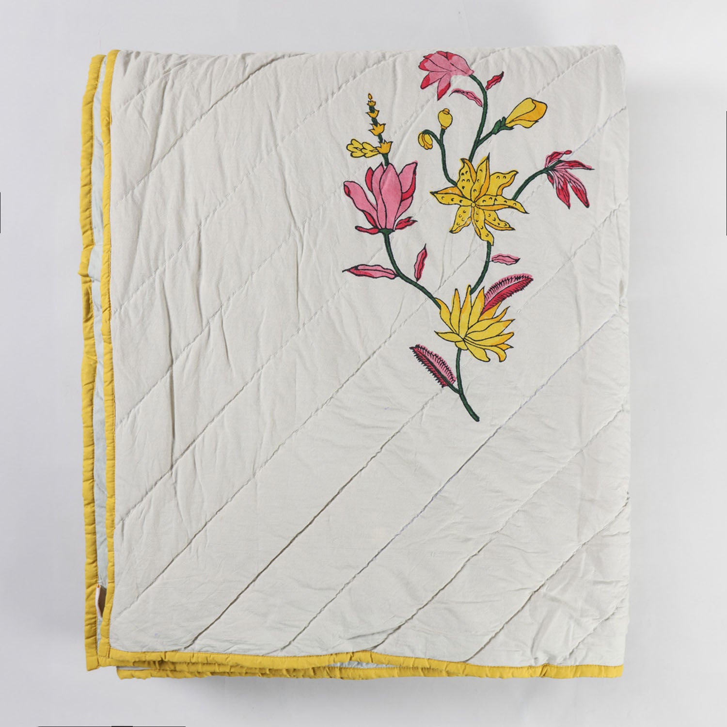 Folded hand block printed cotton quilted bedspread neatly stacked to showcase the floral print, quilted texture, and soft breathable cotton fabric