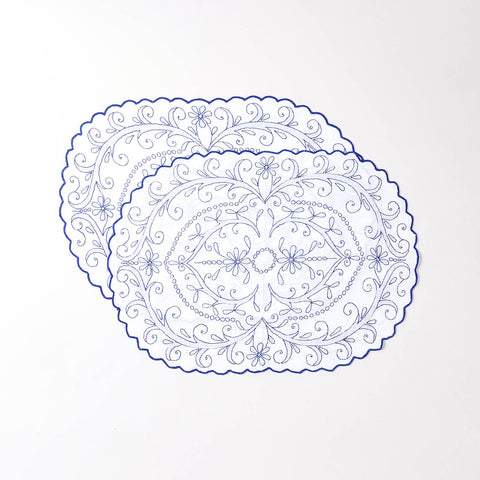 Pair of embroidered cotton table mats featuring blue floral vine motifs and scalloped edges displayed on a plain background