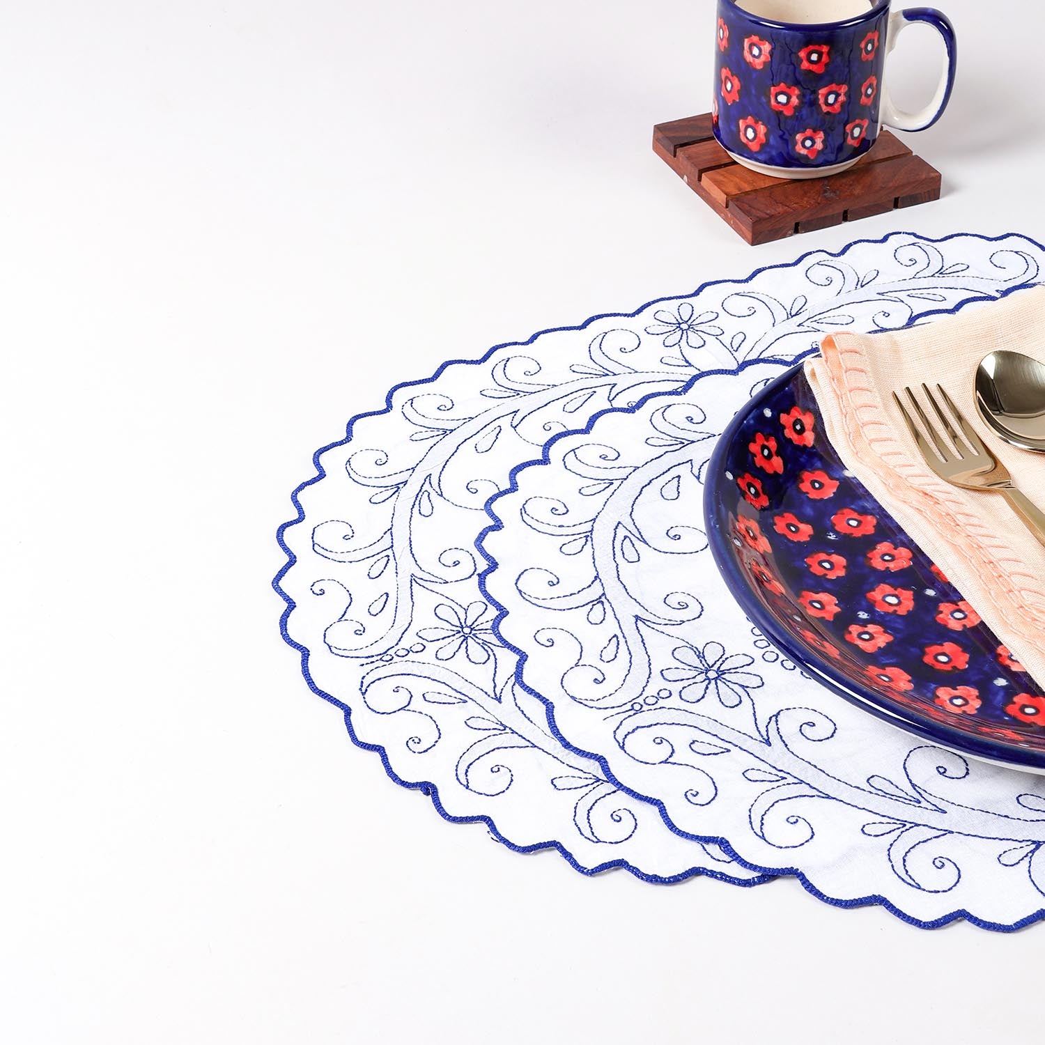 Set of two white cotton table mats with blue chikankari floral embroidery and scalloped edges styled on a dining table, creating an elegant table setting