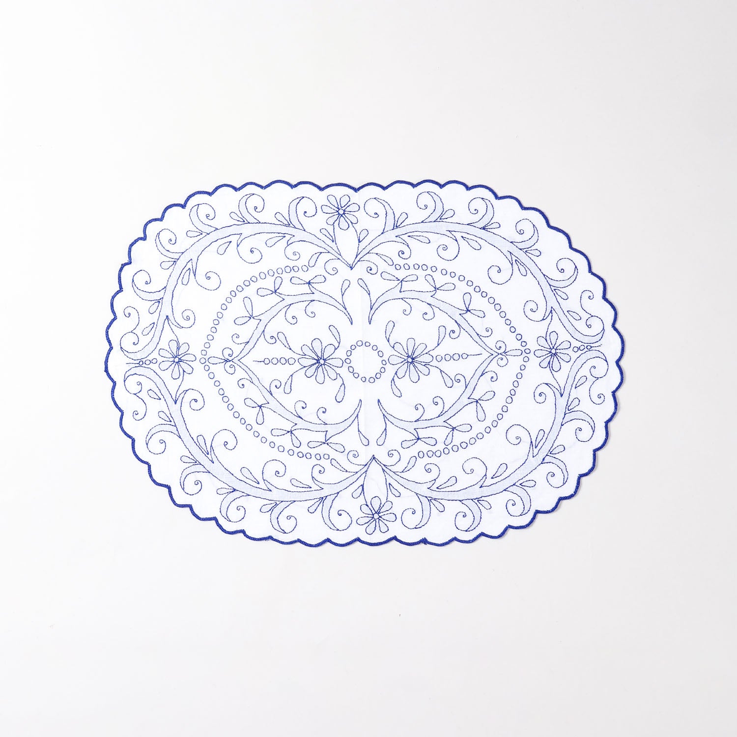 White cotton place mat with blue hand embroidery, floral vine patterns, and decorative scalloped edges