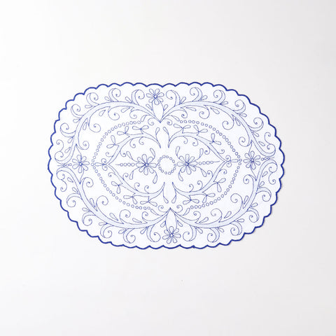 White cotton place mat with blue hand embroidery, floral vine patterns, and decorative scalloped edges