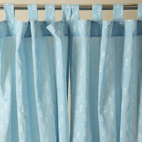 Hand dyed blue mulmul cotton curtain with hand block printed fish motifs hanging by a window