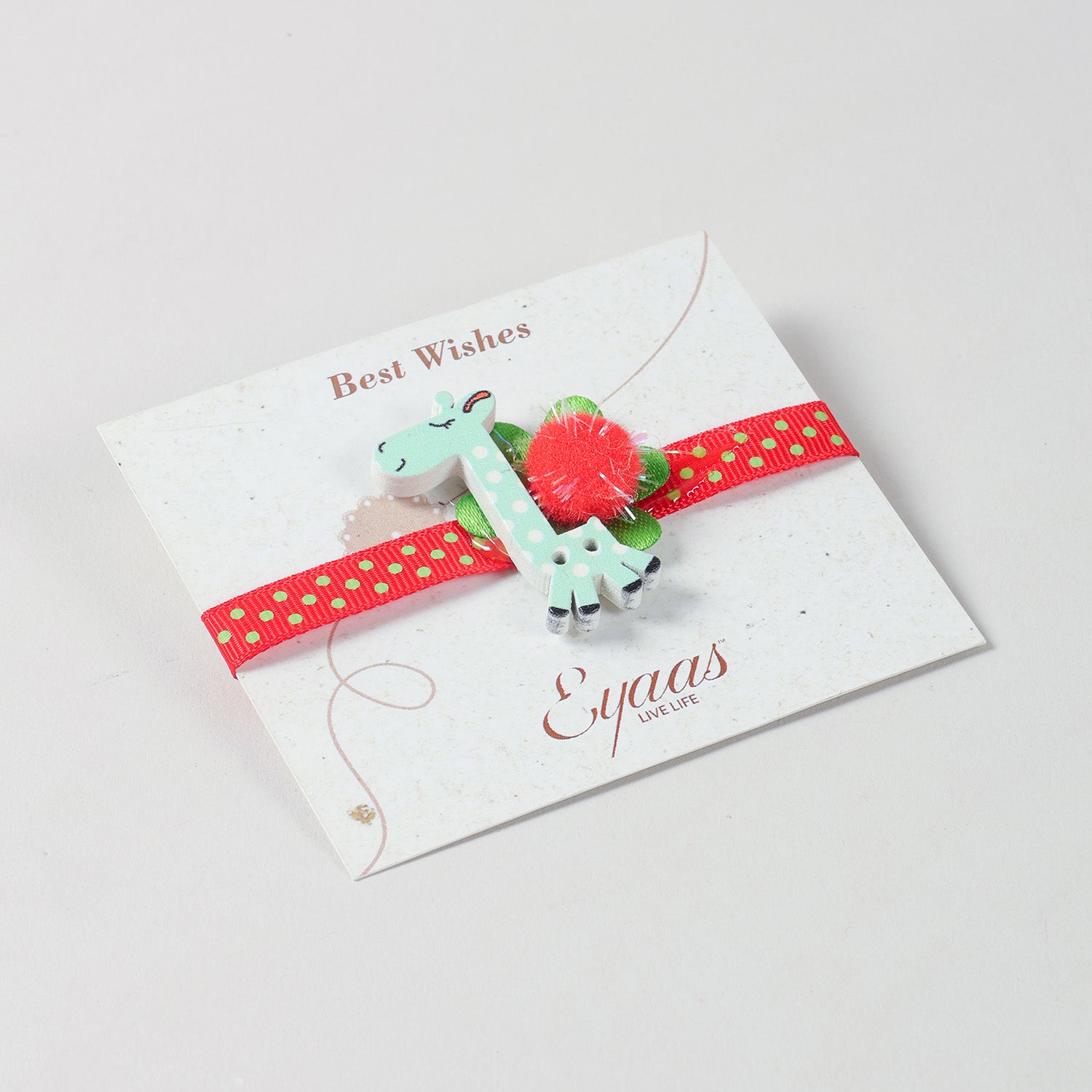 Angled view of the handmade Blue Giraffe Wooden Kids Rakhi with red ribbon attached to a festive Best Wishes card for Raksha Bandhan gifting
