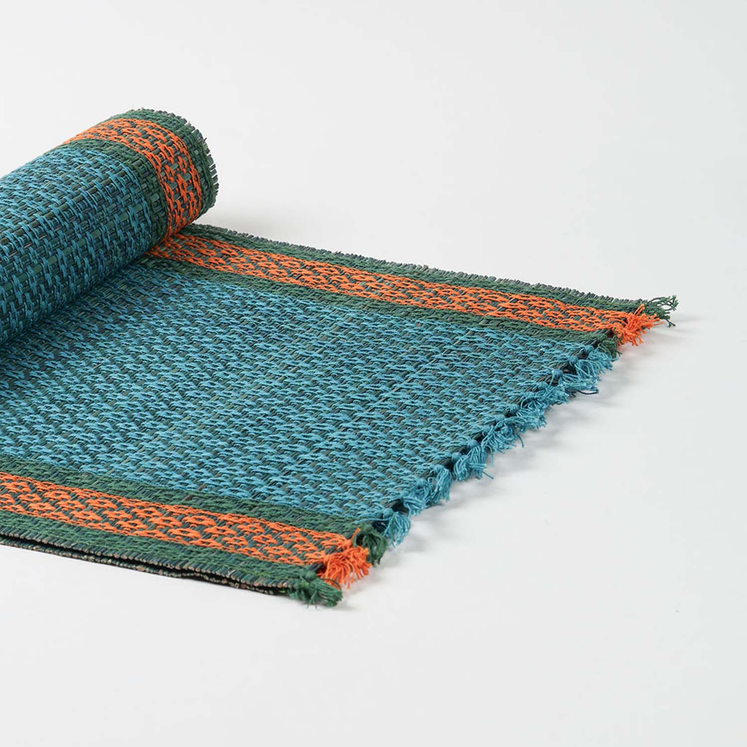 Angled view of a handmade blue Madurkathi table runner highlighting flexible natural fibre weaving and colourful border accents