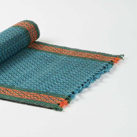 Angled view of a handmade blue Madurkathi table runner highlighting flexible natural fibre weaving and colourful border accents