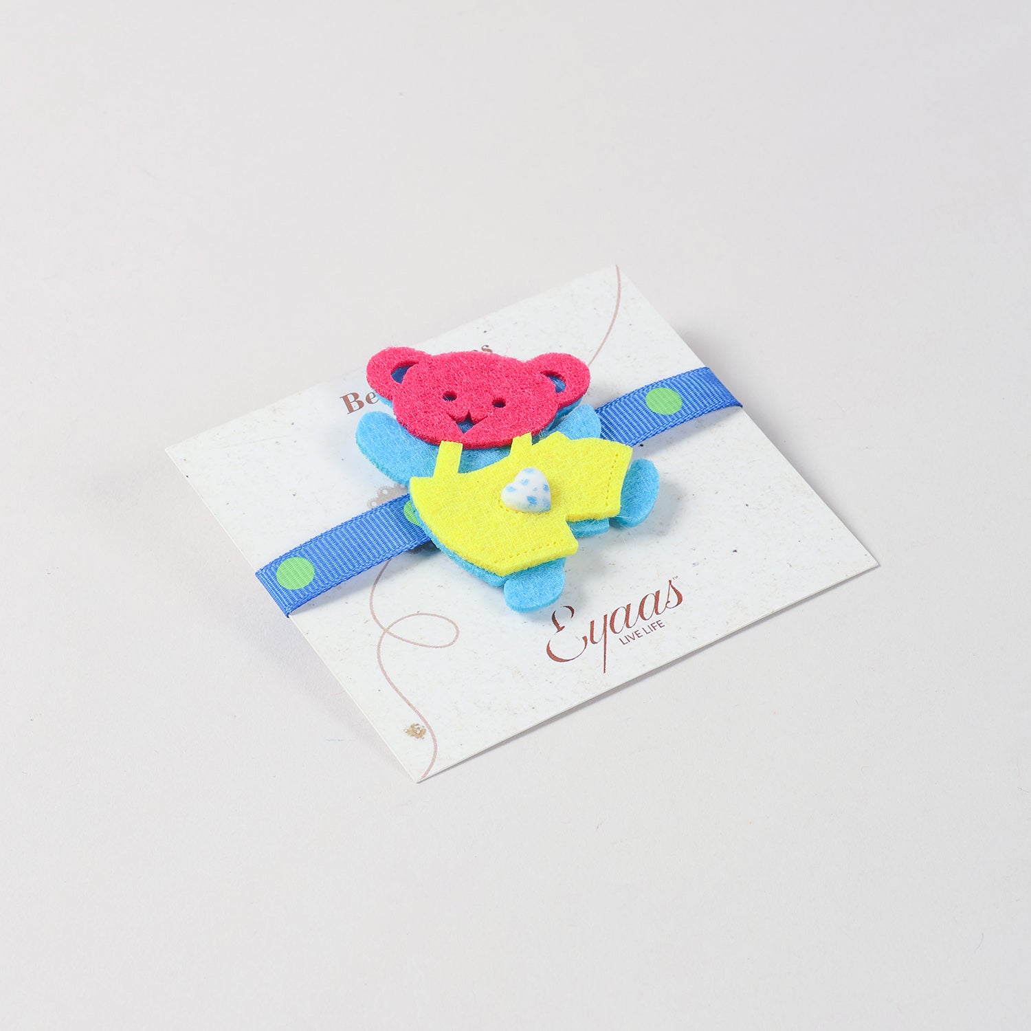 Angled view of the handmade blue and yellow Teddy Bear Felt Kids Rakhi attached to a festive Best Wishes card for Raksha Bandhan gifting