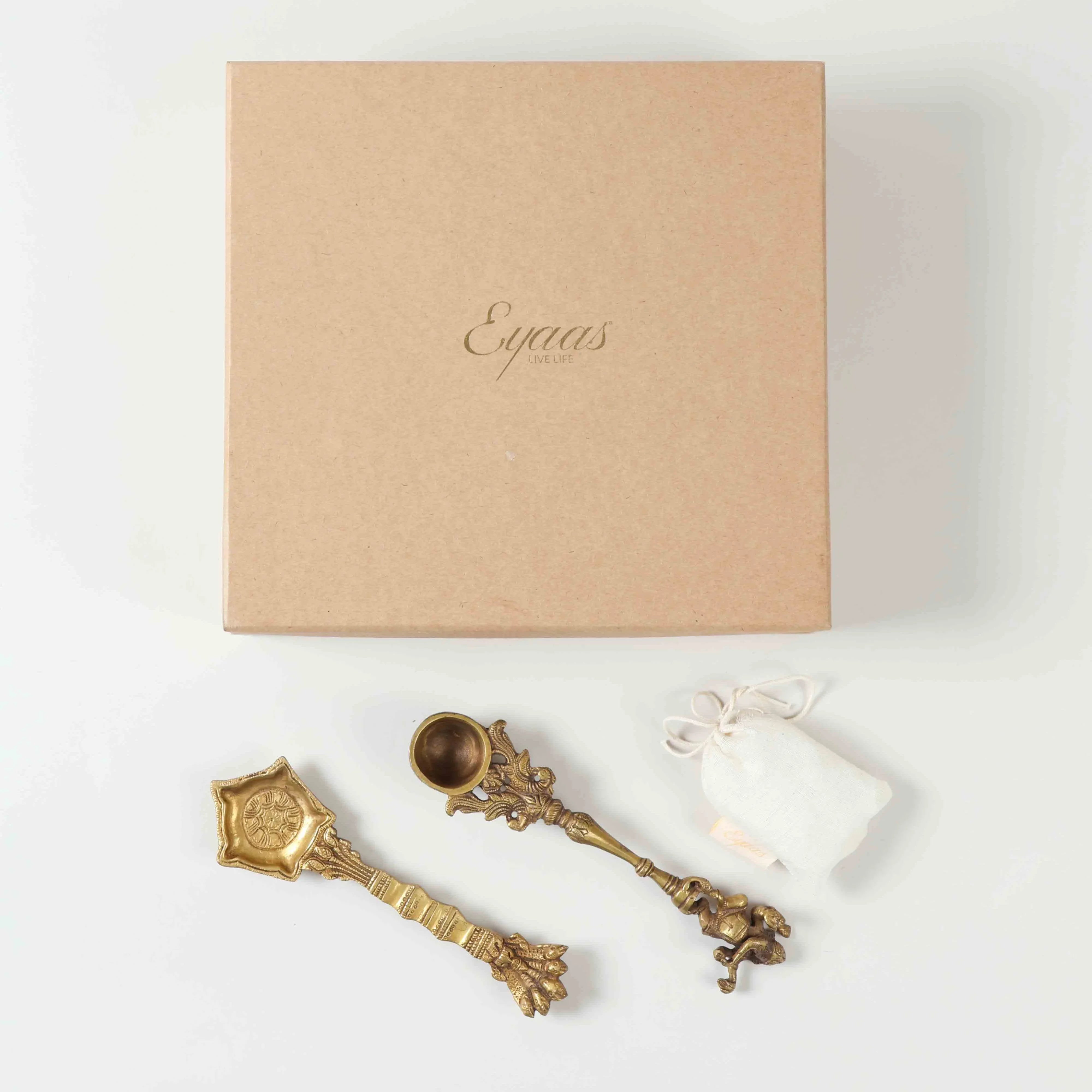 Top view of a pooja ritual gift set featuring two brass hawan spoons and Kapoor displayed together against a clean background