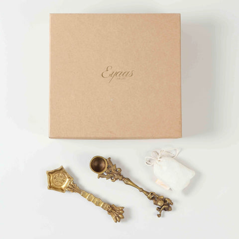 Top view of a pooja ritual gift set featuring two brass hawan spoons and Kapoor displayed together against a clean background