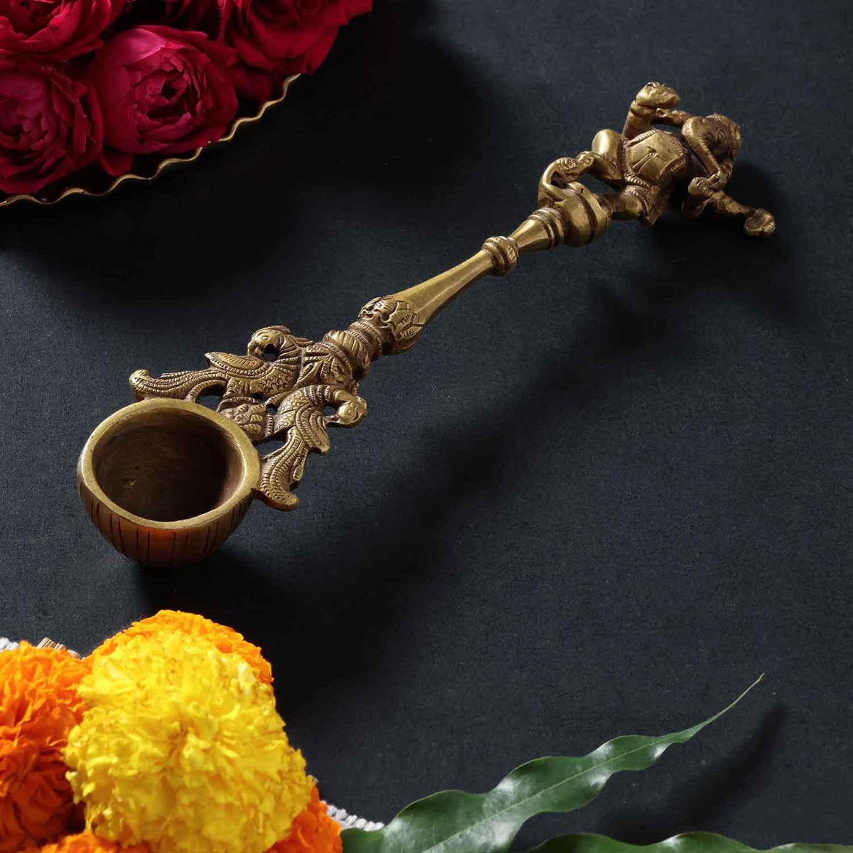 Brass hawan spoon with  Dancing Ganesha  motif handle styled in a traditional puja setup, showcasing spiritual and festive use