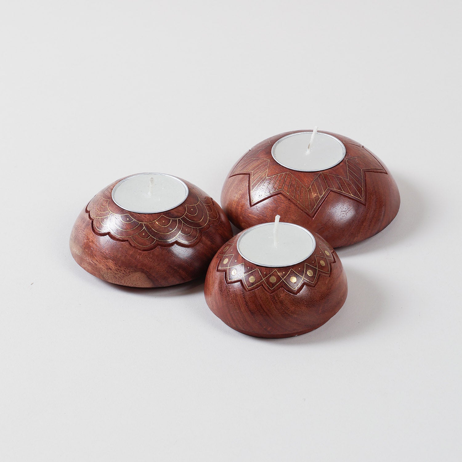 Angled view of a brass inlay wooden T-light holder set showcasing handcrafted star, lotus, and scalloped designs in varying sizes