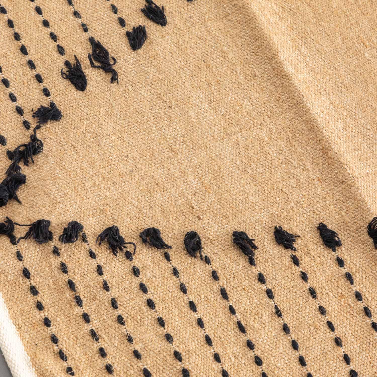 Close-up of black dotted stripe patterns on a brown handwoven cotton dhurrie rug, highlighting artisan craftsmanship
