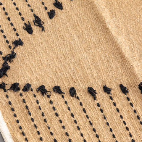 Close-up of black dotted stripe patterns on a brown handwoven cotton dhurrie rug, highlighting artisan craftsmanship