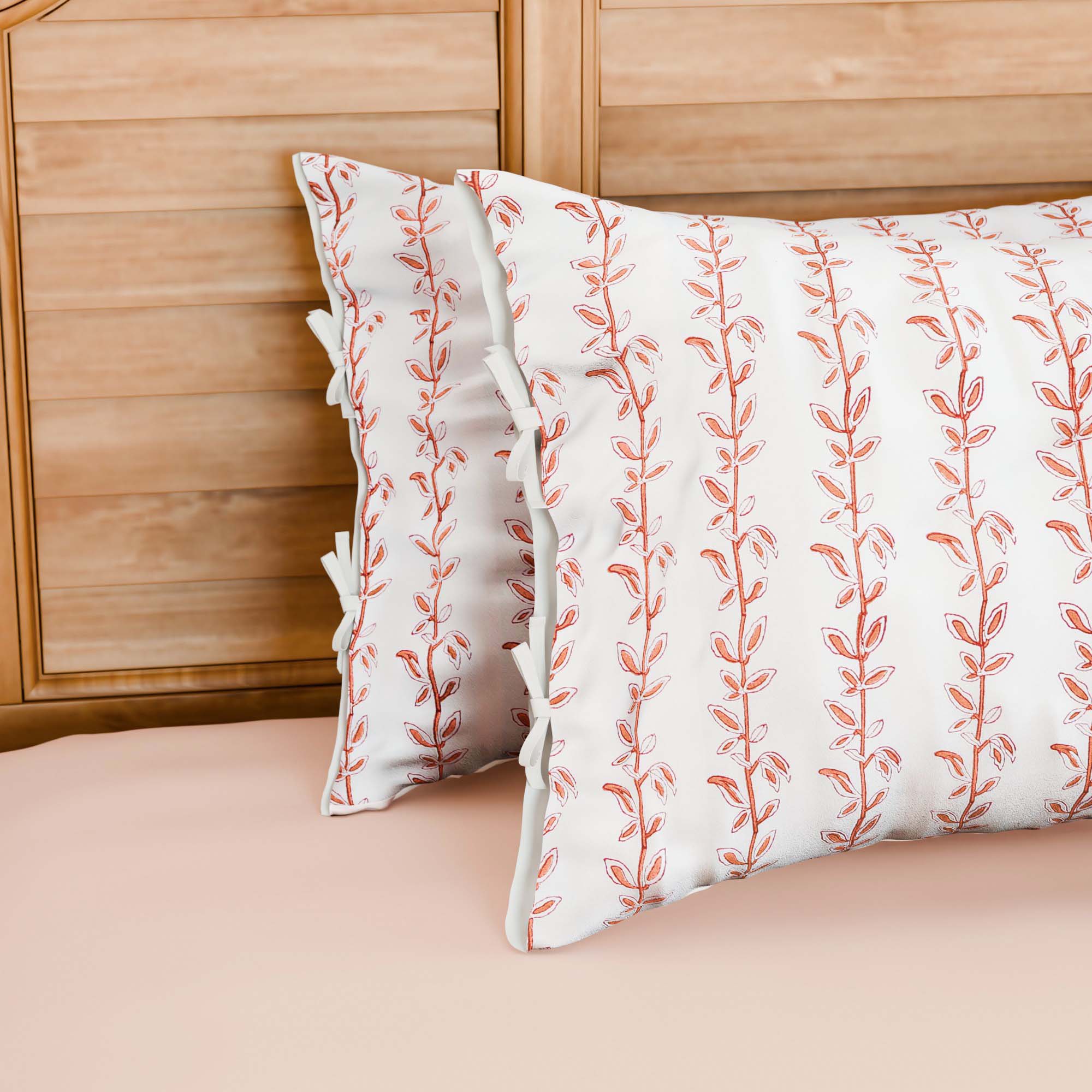 Hand block printed cotton pillow cover set with brown and red climbing vine motifs on a white base, styled on a bed with coordinated cotton bed linen