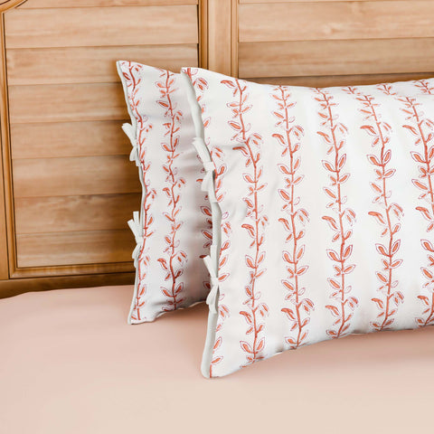 Hand block printed cotton pillow cover set with brown and red climbing vine motifs on a white base, styled on a bed with coordinated cotton bed linen