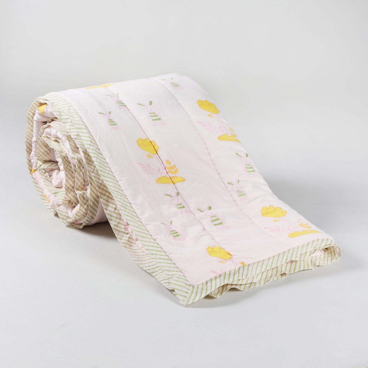 Rolled 60x90 reversible cotton quilt featuring playful bunny and tree motifs in pastel colours on a light pink background