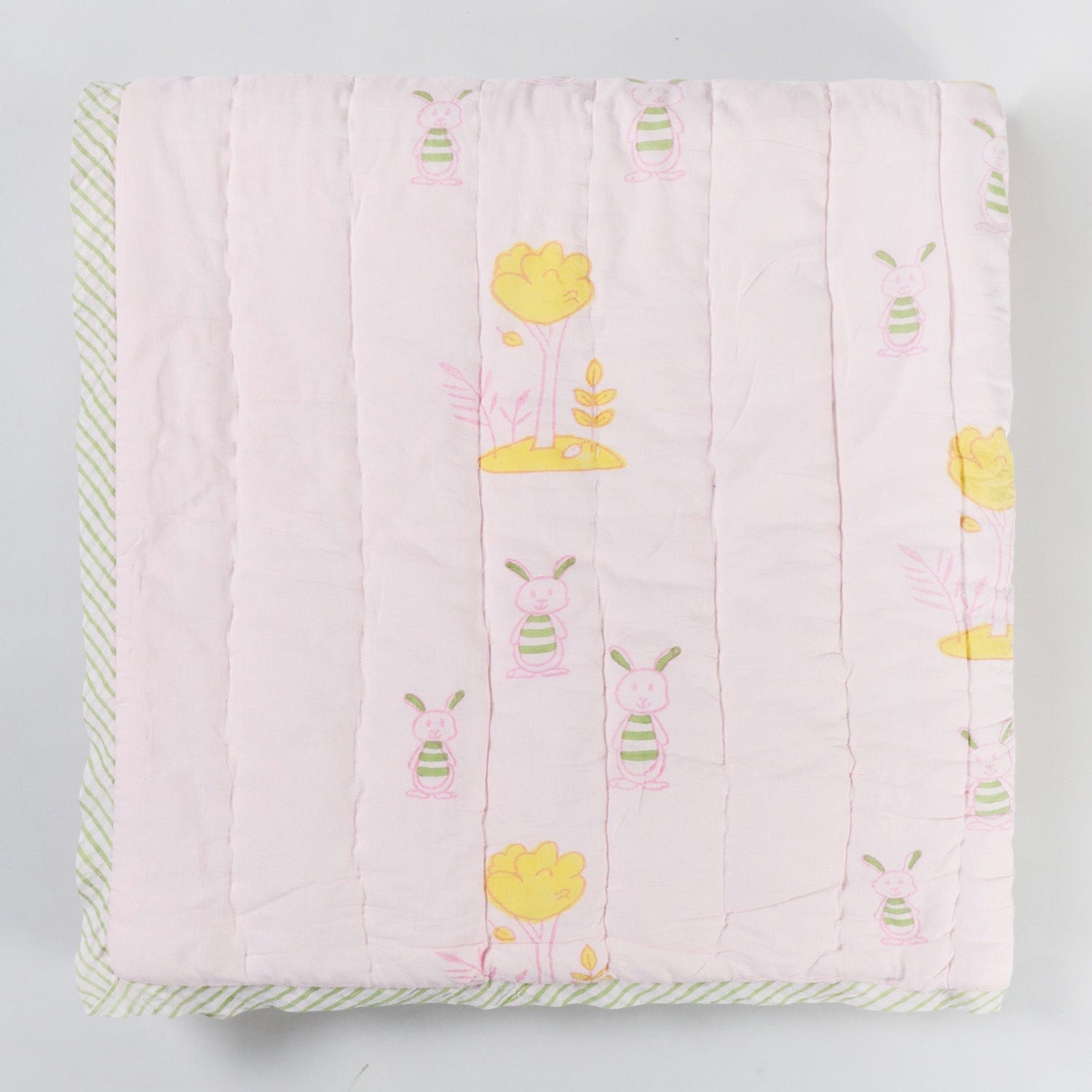 Folded hand block printed cotton quilt showcasing bunny and tree motifs, soft cotton fabric, and reversible construction