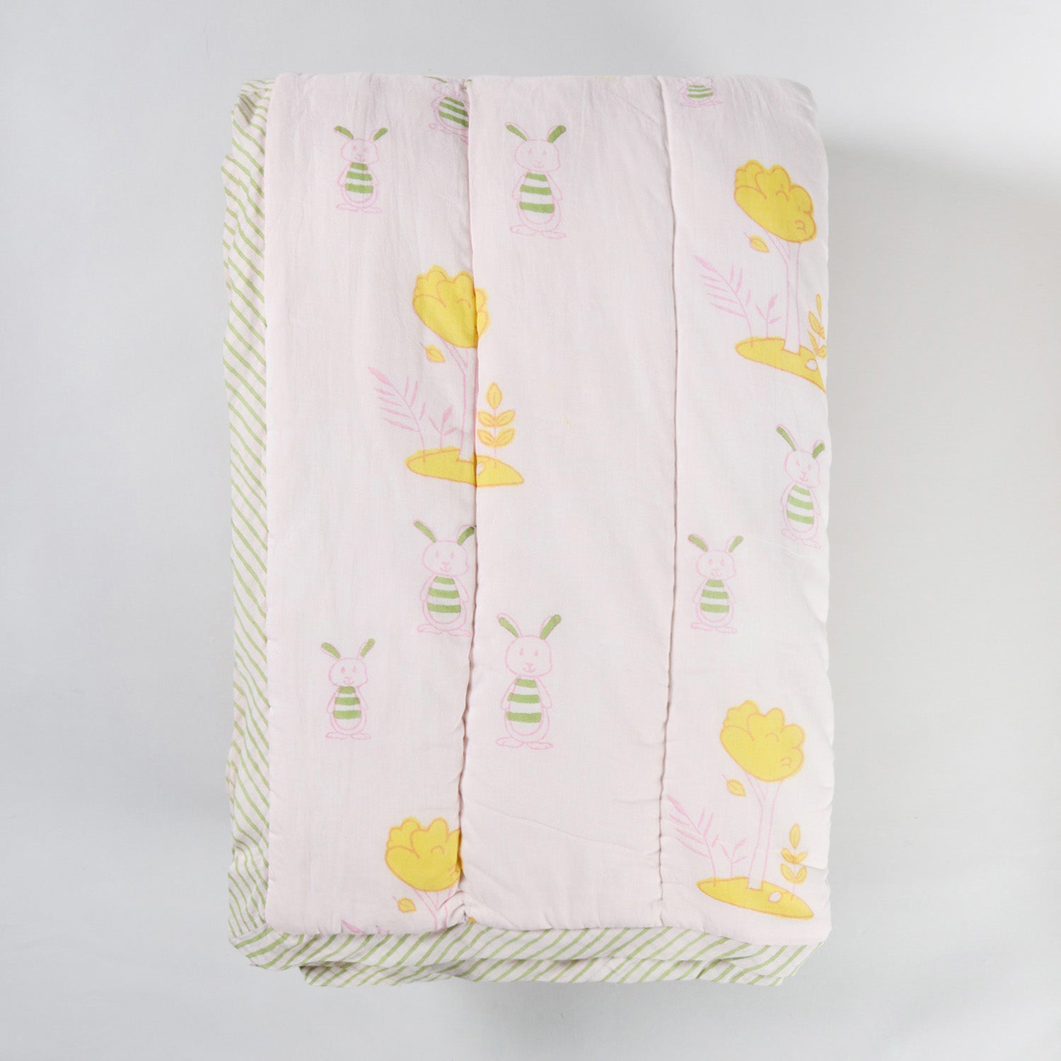 Folded hand block printed cotton quilt with bunny and tree designs, highlighting its soft texture and reversible construction