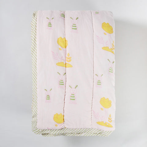 Folded hand block printed cotton quilt with bunny and tree designs, highlighting its soft texture and reversible construction