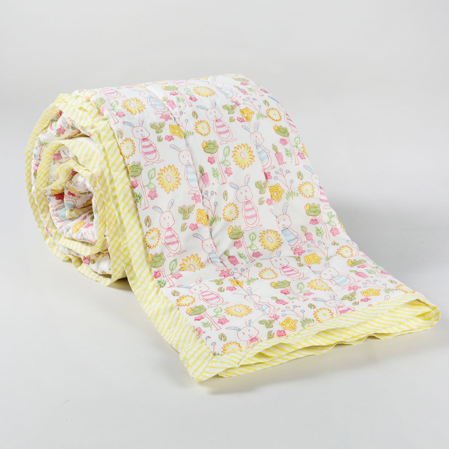 a 60x90 reversible cotton quilt with bunny garden block print motifs on a white base in soft multicolour shades kept in rolled position