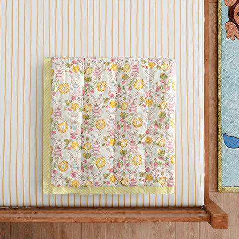 Styled close-up of a hand block printed cotton quilt with bunny and garden motifs, highlighting soft cotton texture and multicolour detailing
