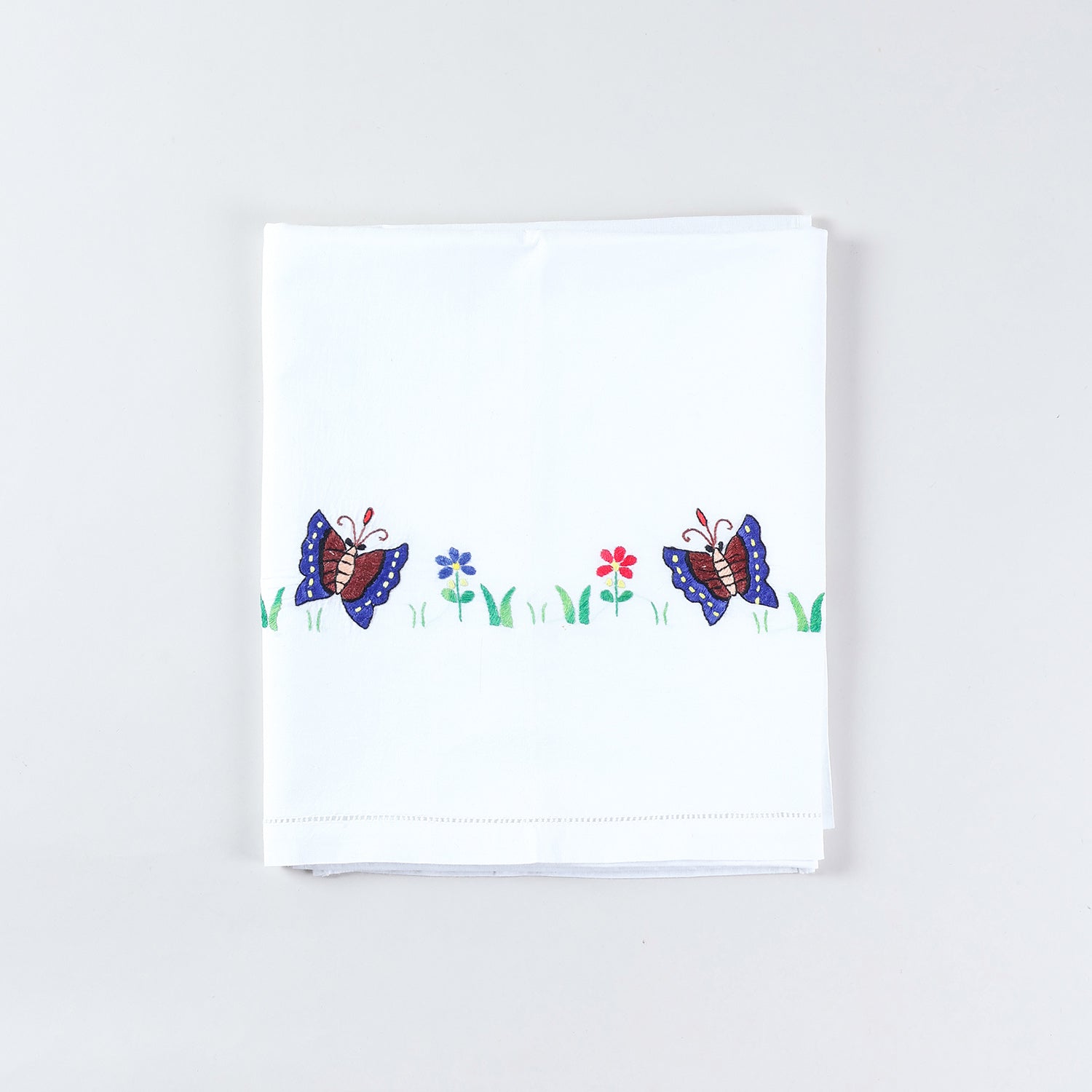 Folded cotton kids bedsheet and pillow cover set featuring colourful butterfly and flower hand embroidery on a white cotton base