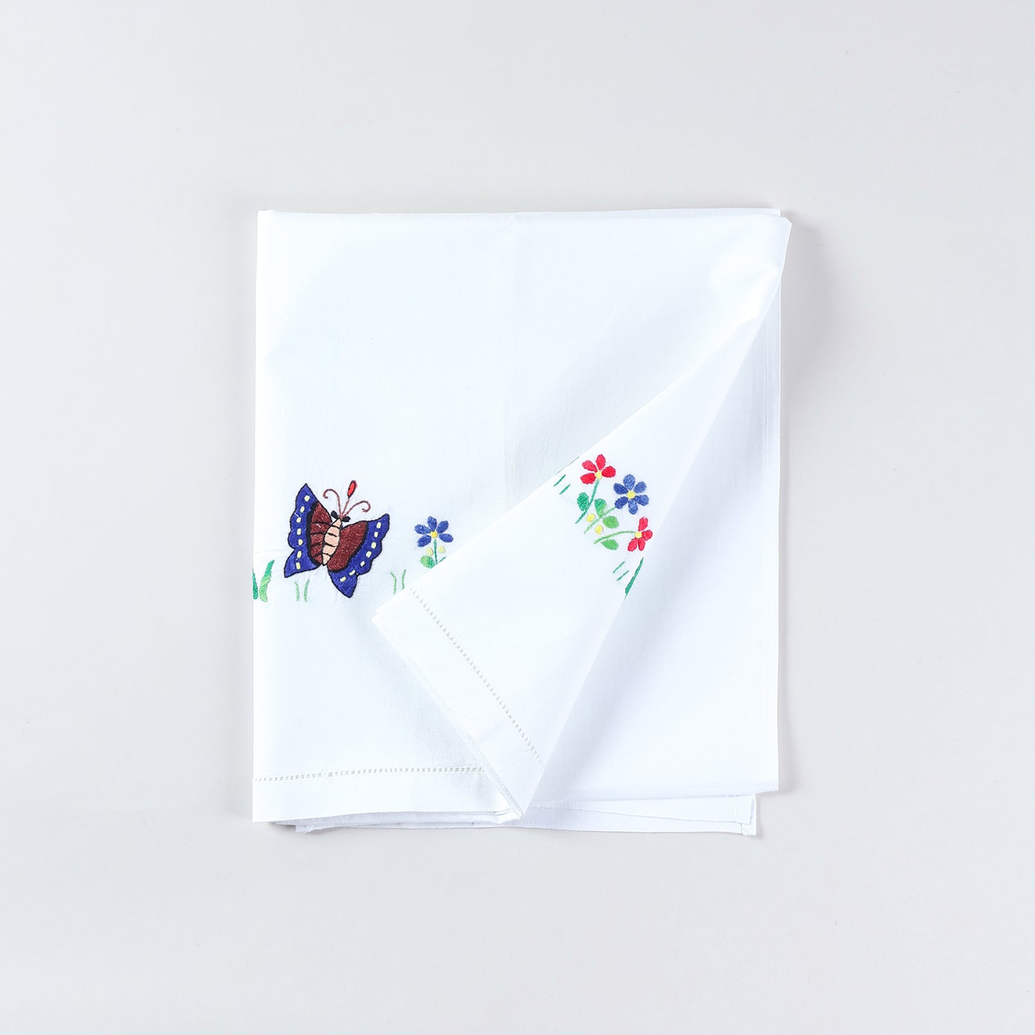 White cotton kids bedsheet folded back diagonally to showcase  butterfly and floral embroidery motifs handcrafted on a soft cotton base