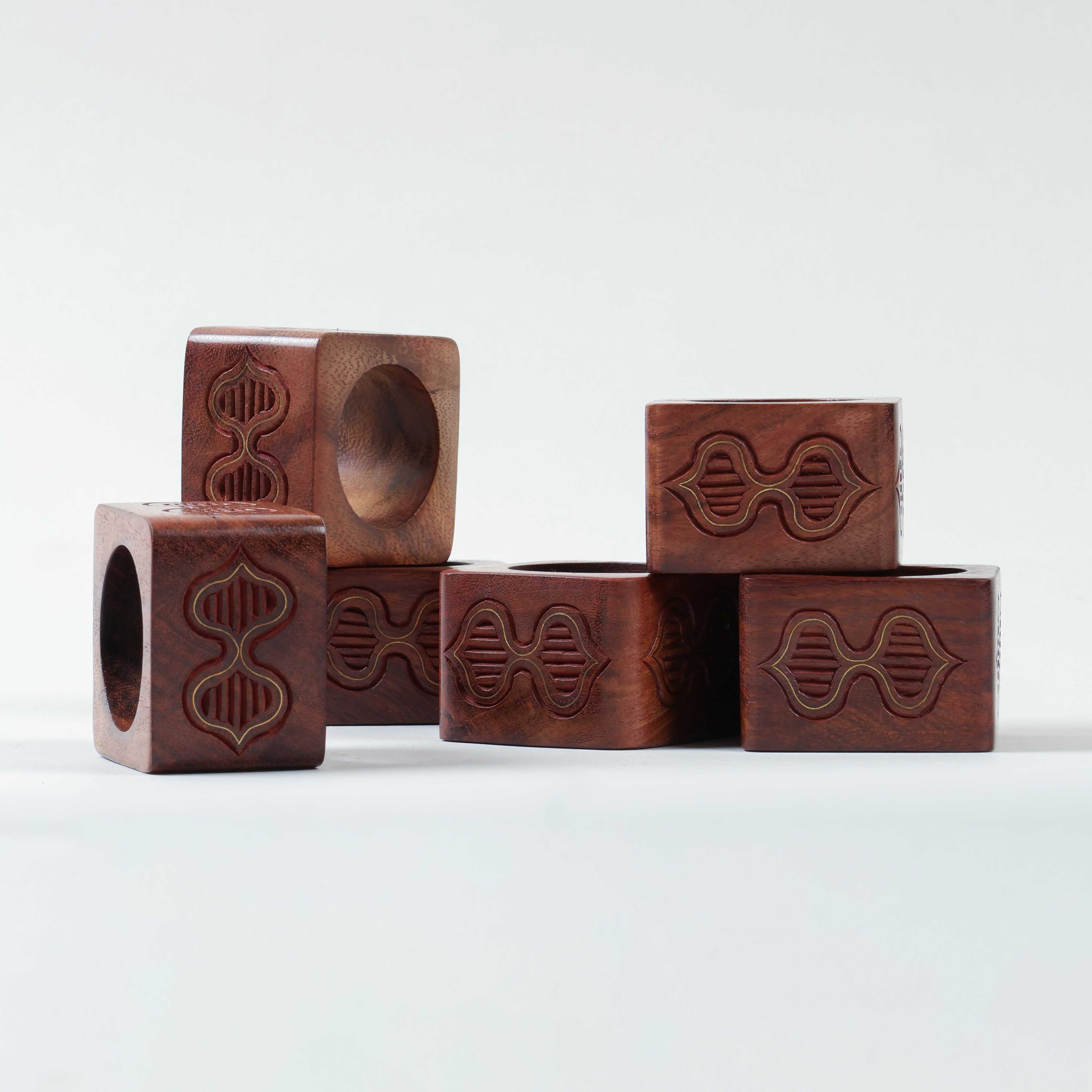 Side view of stacked six wooden napkin rings showcasing butterfly-inspired carving and brass detailing