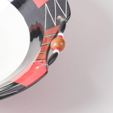 Close-up of a hand-painted ceramic bowl showcasing decorative wooden beads, wire detailing, and intricate African geometric patterns