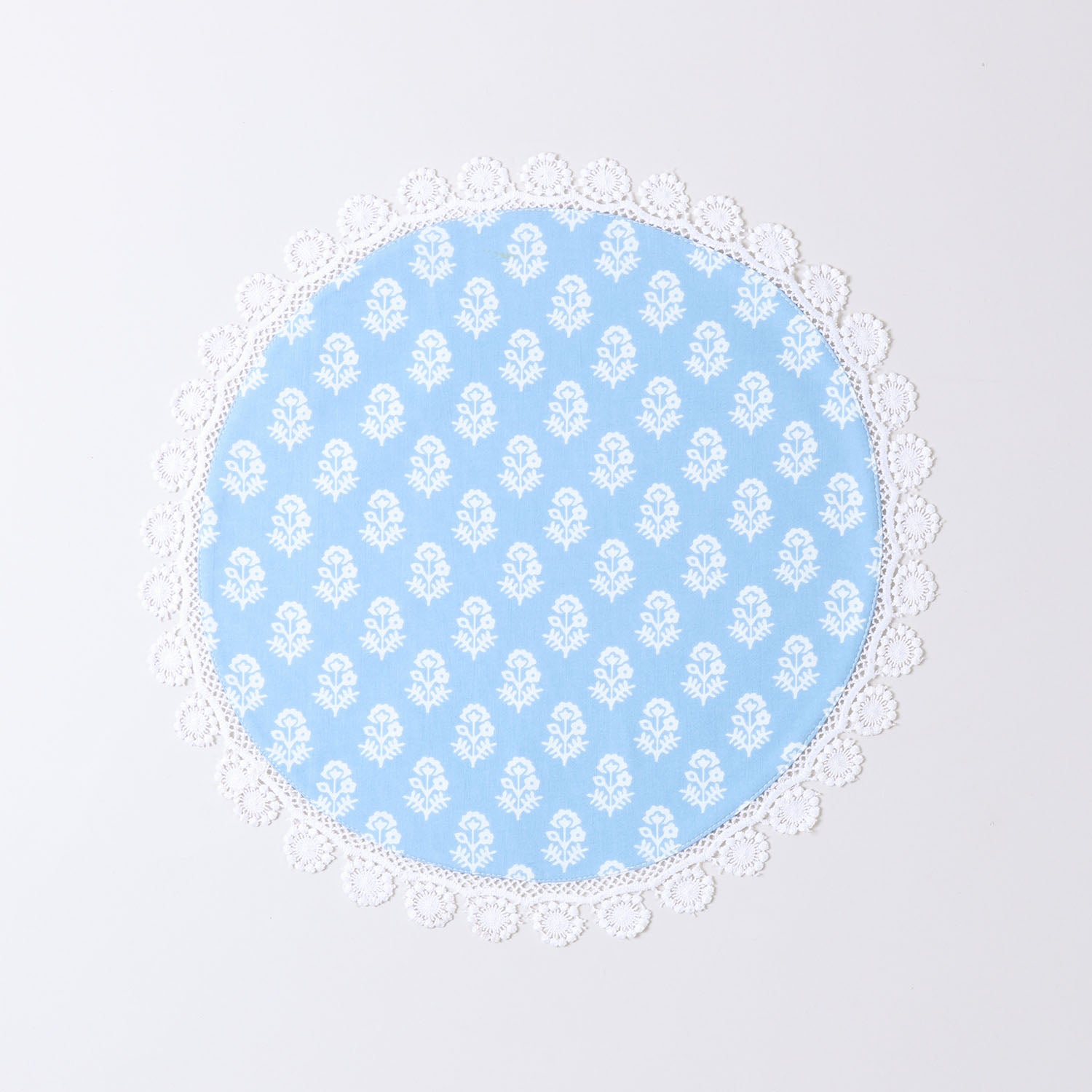 Angled view of a Christmas-themed round placemat showcasing white block printed motifs, blue cotton fabric, and lace trim detailing