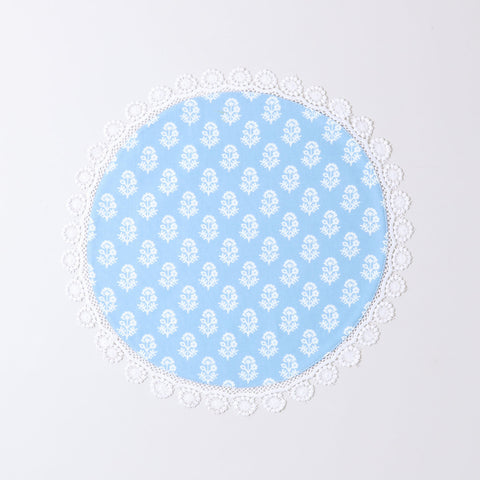 Angled view of a Christmas-themed round placemat showcasing white block printed motifs, blue cotton fabric, and lace trim detailing