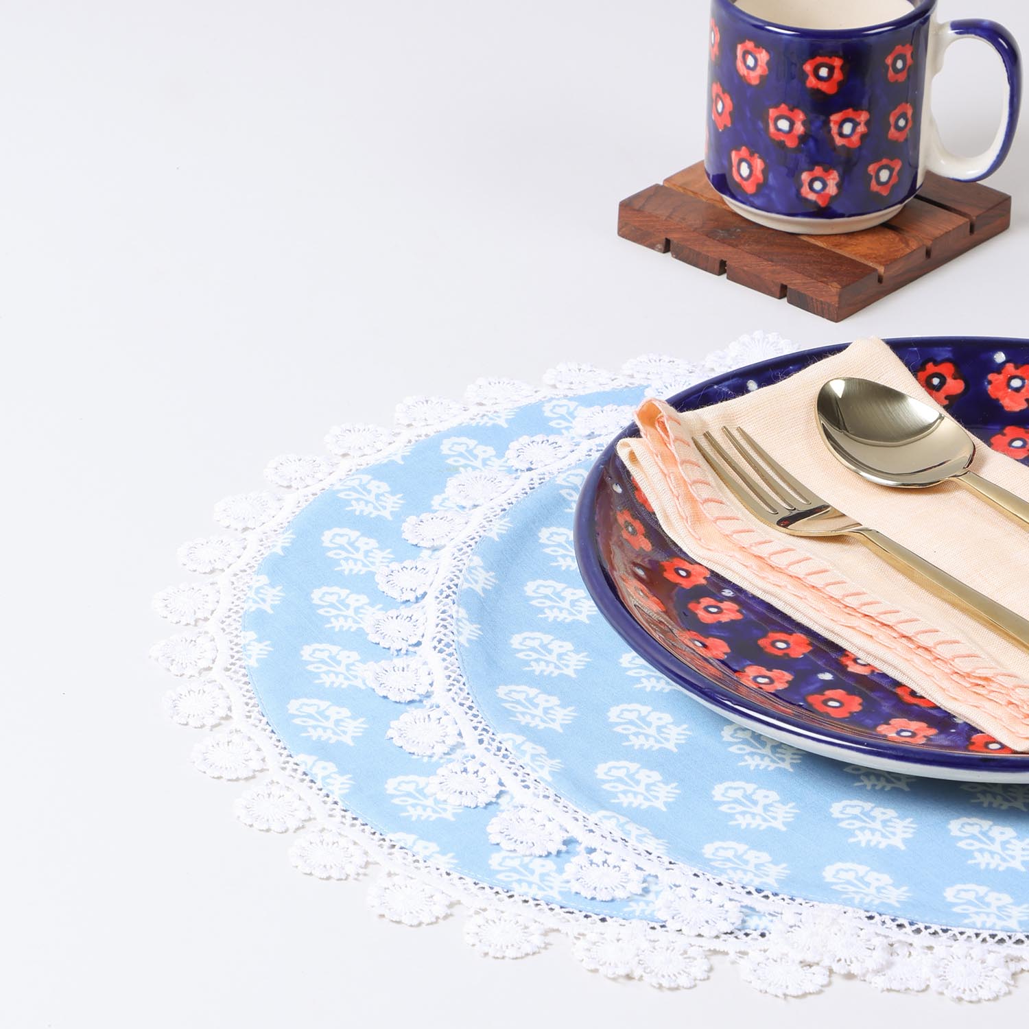 Set of two Christmas-themed round cotton placemats with white block prints on a sky blue base and lace borders styled on a festive dining table setting