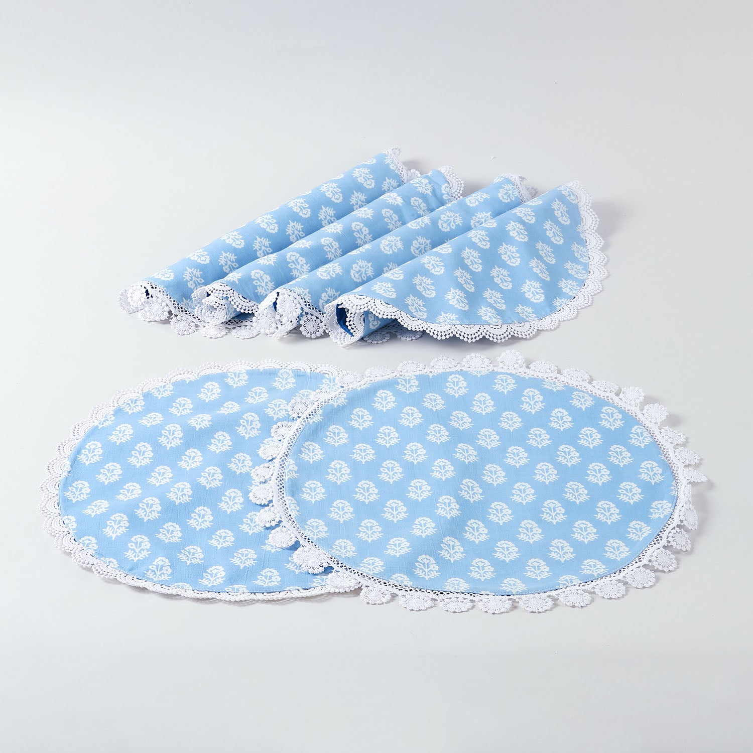 Set of six round cotton Christmas placemats with festive white block prints and lace borders arranged together on a plain background