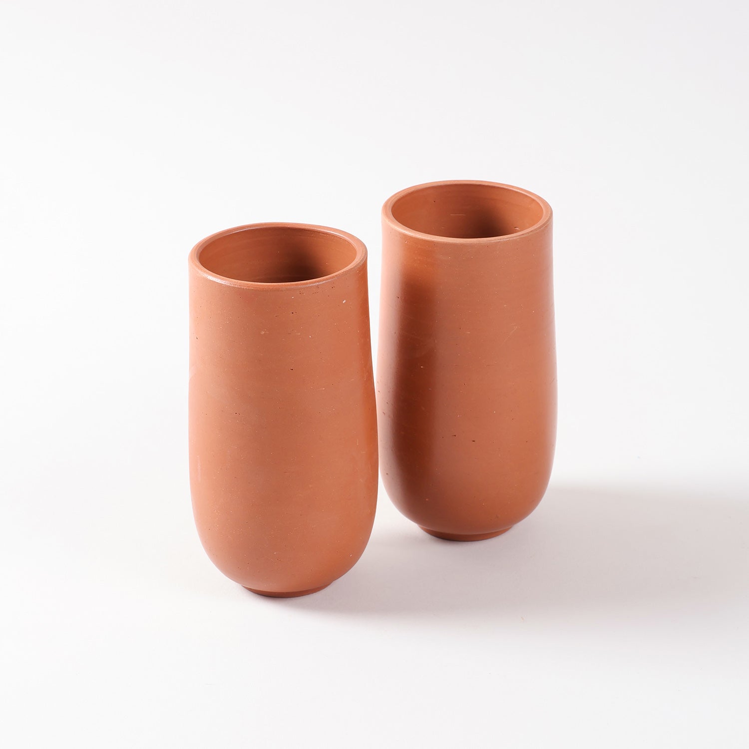 Set of two handmade terracotta tumblers with a curved base and natural clay finish displayed on a plain background