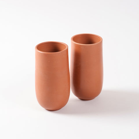 Set of two handmade terracotta tumblers with a curved base and natural clay finish displayed on a plain background