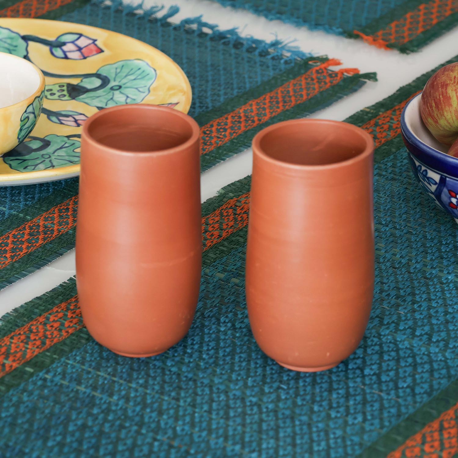 Handmade terracotta glass set of 2 styled on a dining table, featuring naturally cooling clay tumblers for everyday drinks