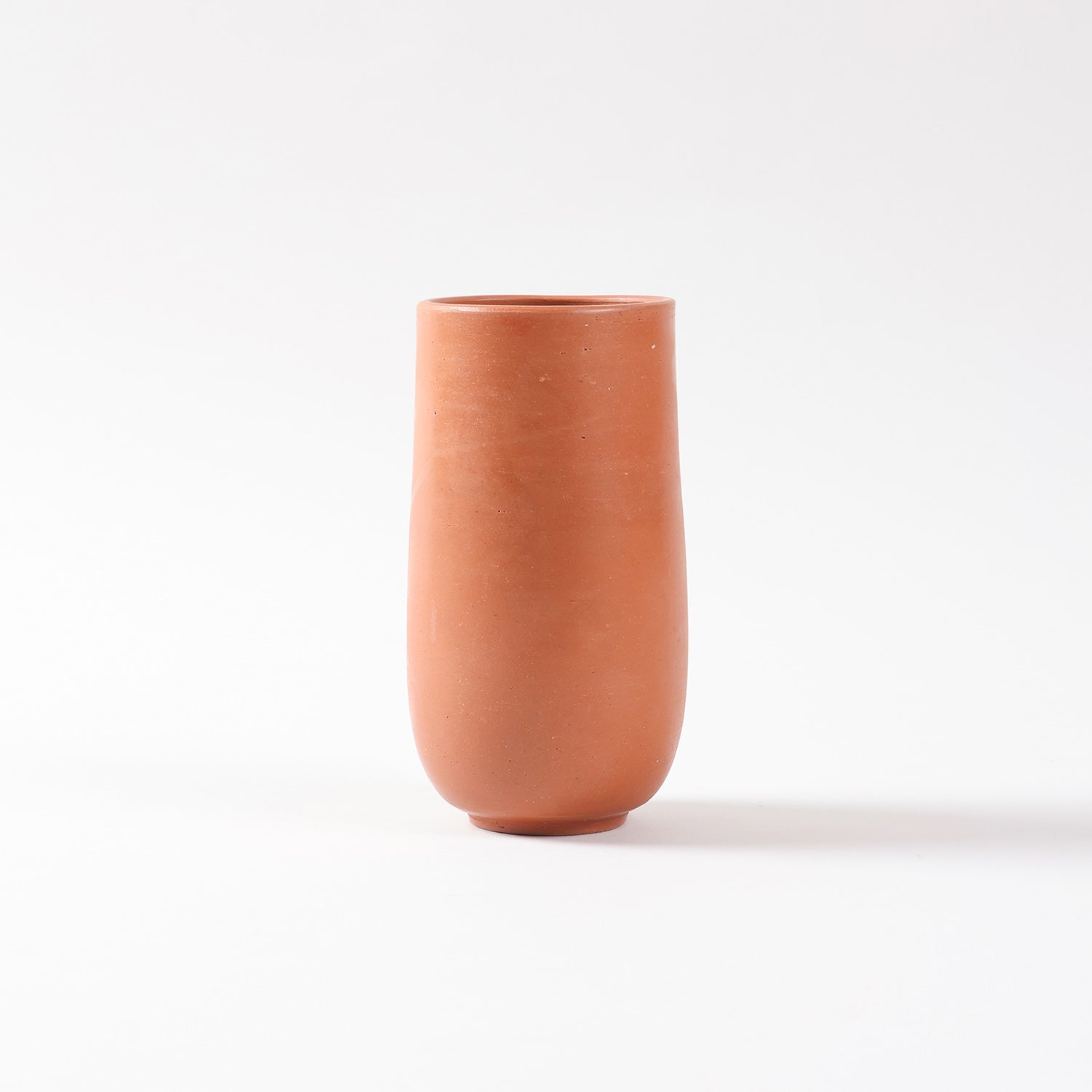Side profile of a handmade terracotta glass highlighting the curved base, smooth clay finish, and traditional craftsmanship