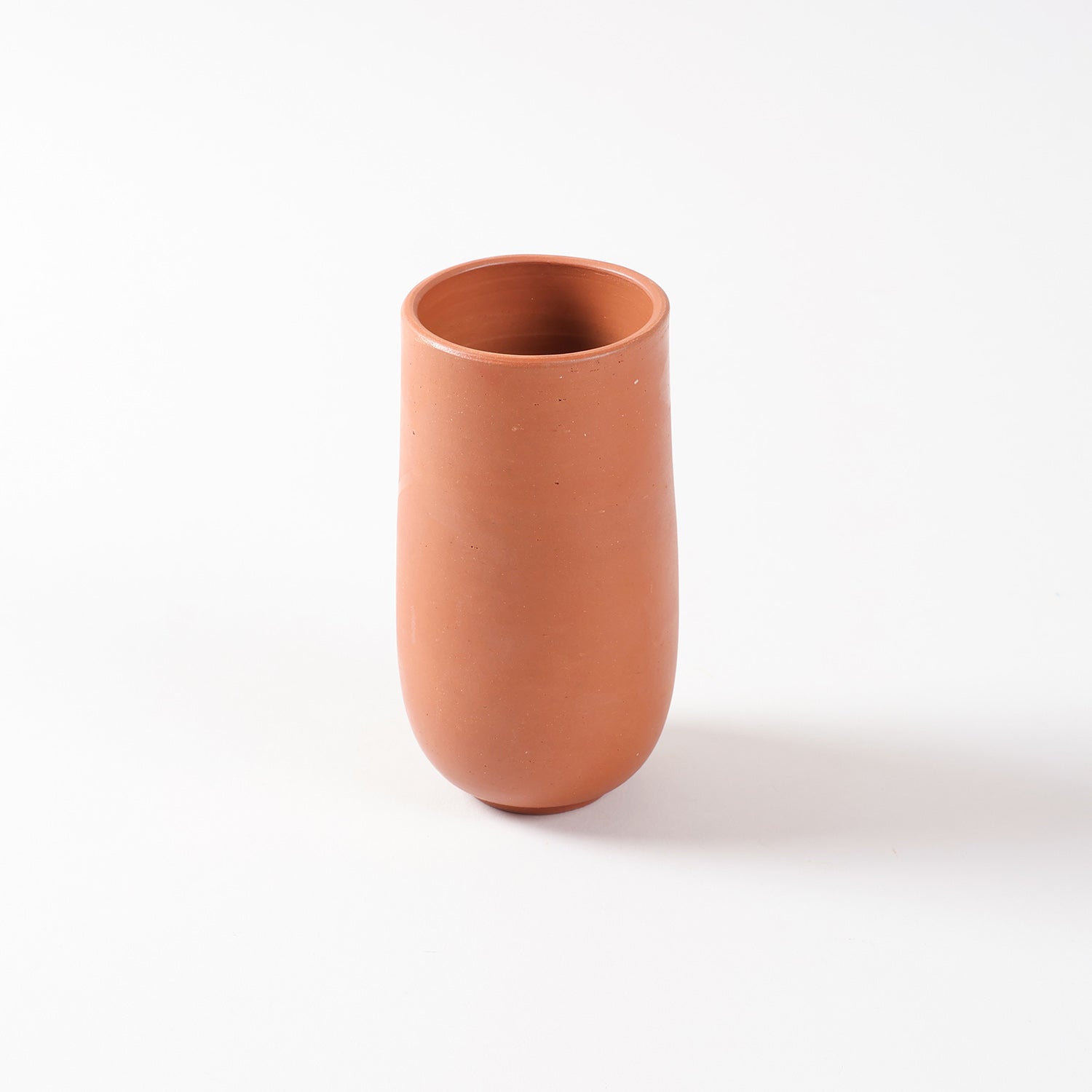 Single terracotta tumbler with a curved base and cylindrical shape, handcrafted from natural clay for cool beverages