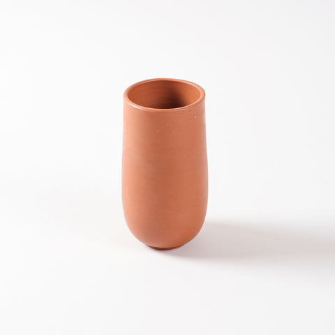 Single terracotta tumbler with a curved base and cylindrical shape, handcrafted from natural clay for cool beverages